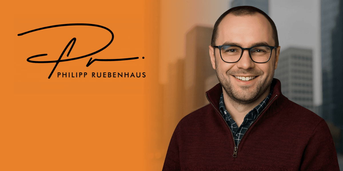 Professional portrait of a smiling man in a burgundy sweater with a city backdrop