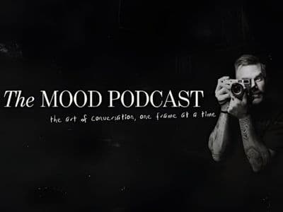 A black-and-white image of a man holding a camera, with 'The MOOD Podcast' title and tagline about creative conversations.