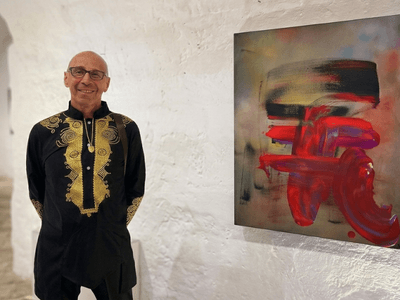 Marc Noël standing beside a vibrant abstract quantum painting at a contemporary art exhibition.