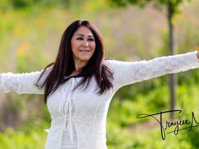 A woman stands in grass with arms outstretched, embodying openness and connection in a natural setting.