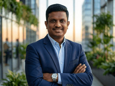 Businessman in suit smiling with arms crossed in modern office corridor with plants and glass walls.