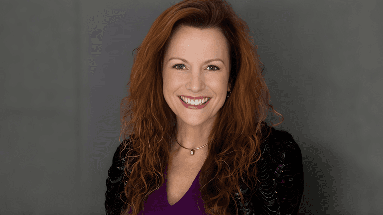 Nancy Prince, experienced real estate leader, smiling while holding a business report, reflecting leadership and innovation in real estate."