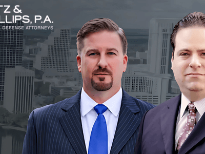 Two suited men in front of a city skyline with the Katz & Phillips, P.A. logo above them.