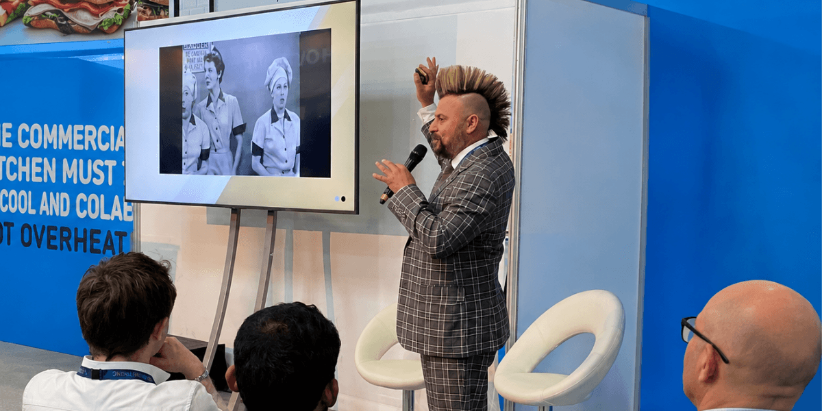 A presenter in a checked suit gestures towards a screen showing vintage images.