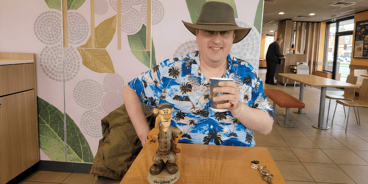 A man in a floral shirt and hat sits at a table with a toy.