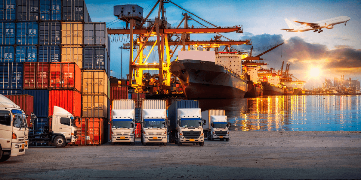Shipping containers and trucks at a busy port with ships and an airplane in the background