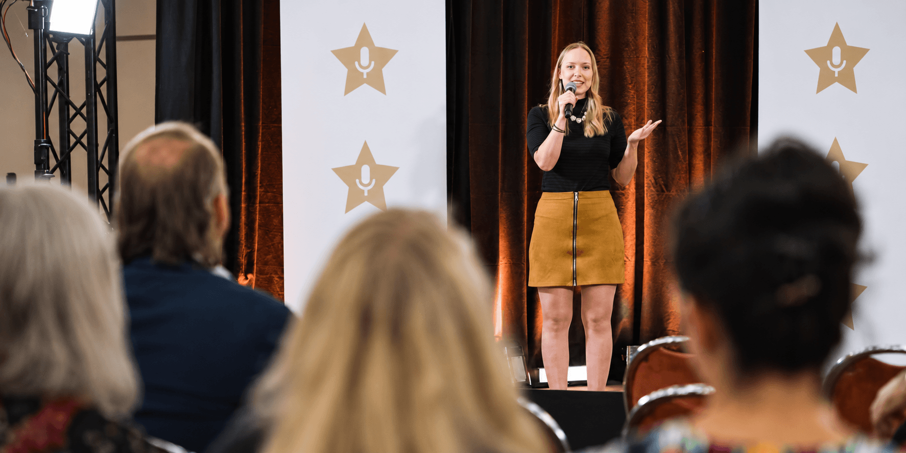 A woman stands on stage speaking to an audience at an event