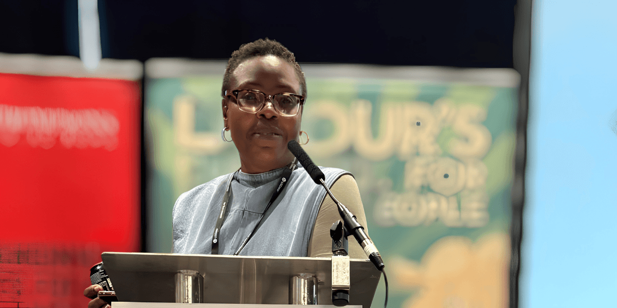 A woman with glasses speaks at a podium during a conference event