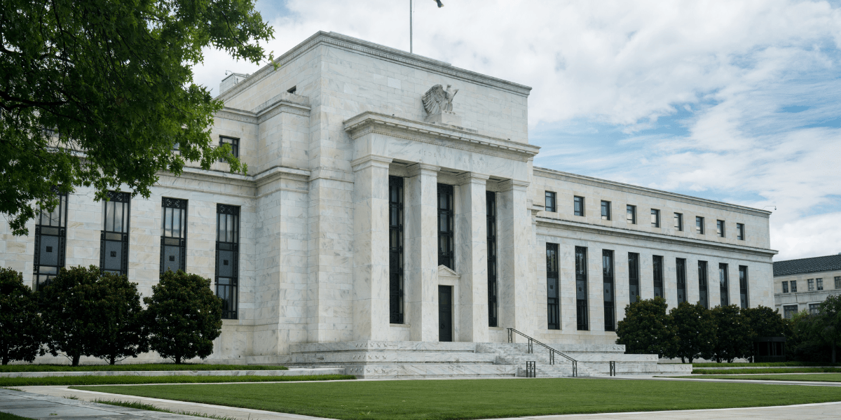Federal Reserve building with marble facade, columns, and flag against a cloudy sky