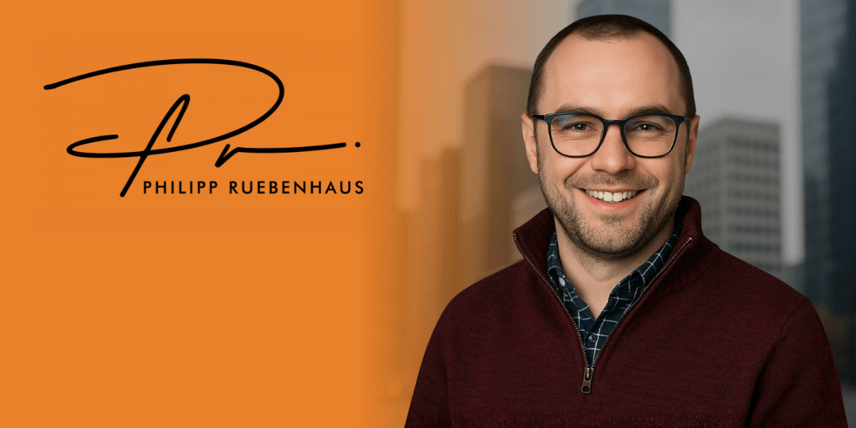 Professional portrait of a smiling man in a burgundy sweater with a city backdrop