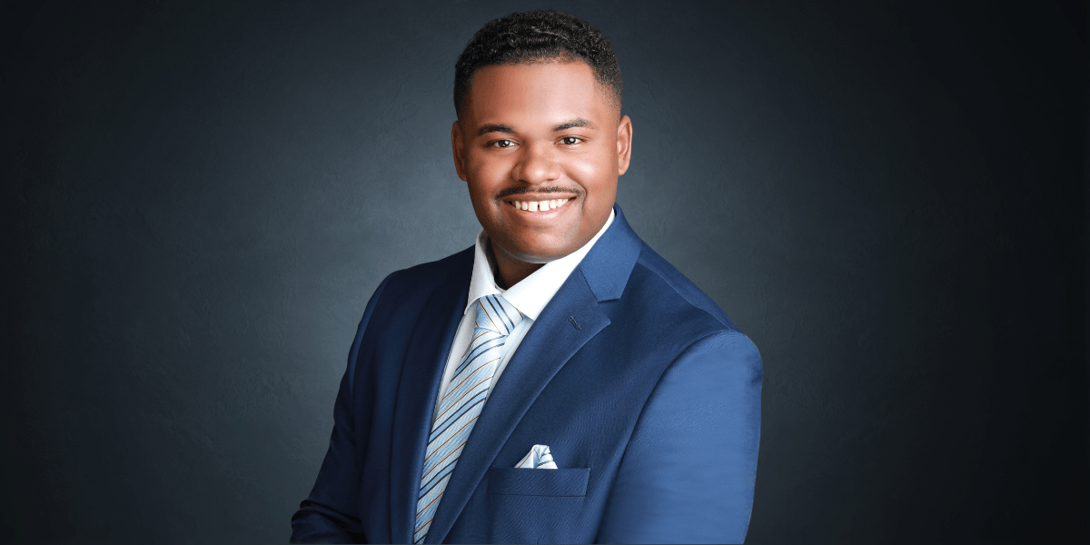 Smiling man in blue suit and tie, professional headshot against dark background.