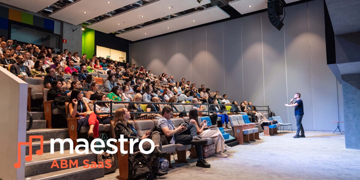Audience watching a presenter in a modern auditorium, with "maestro ABM SaaS" logo in the foreground. The tone is professional and engaging.