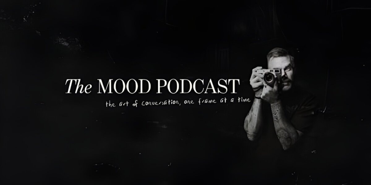 A black-and-white image of a man holding a camera, with 'The MOOD Podcast' title and tagline about creative conversations.