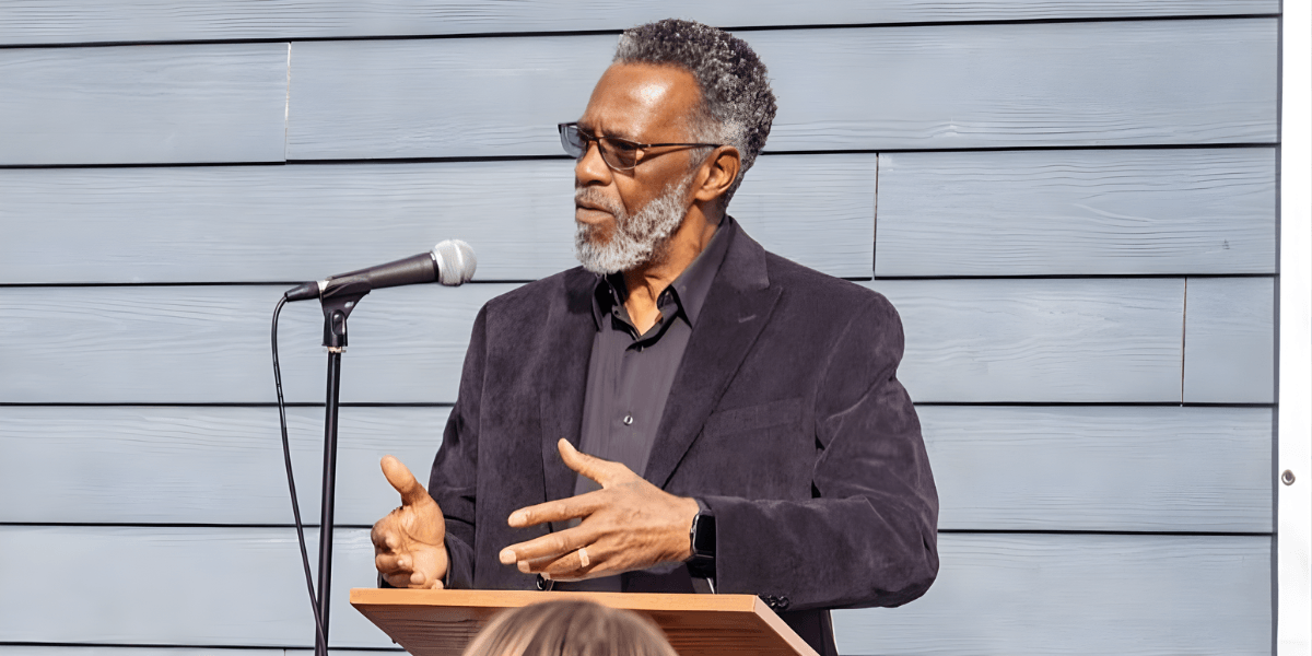 Man speaking at podium with microphone during community event, addressing audience about leadership, unity, and empowerment.