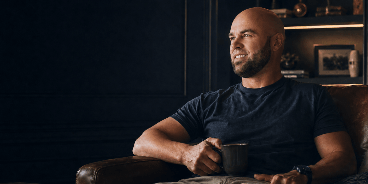 Veteran entrepreneur Adam Jacobs holding a coffee mug in a modern office, representing Astral & Root's wellness mission.