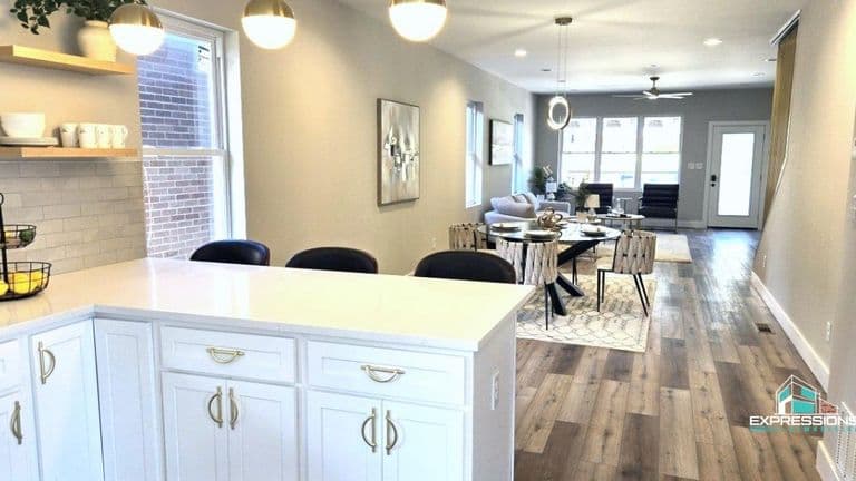Bright, modern kitchen with white cabinetry, quartz countertops, and stylish pendant lights, overlooking a dining and living area with hardwood floors and contemporary furnishings.