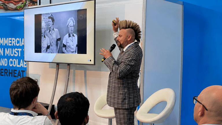 A presenter in a checked suit gestures towards a screen showing vintage images.