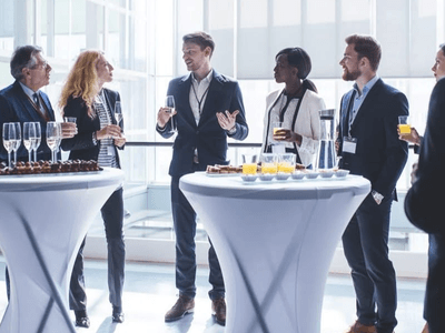A professional gathering with people talking and enjoying drinks at cocktail tables