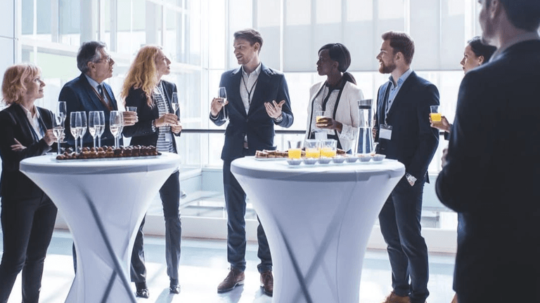 A professional gathering with people talking and enjoying drinks at cocktail tables