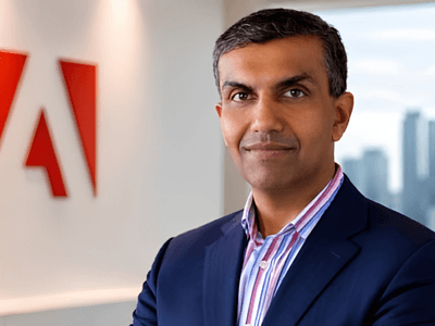 Business professional stands in front of an Adobe logo in an office setting