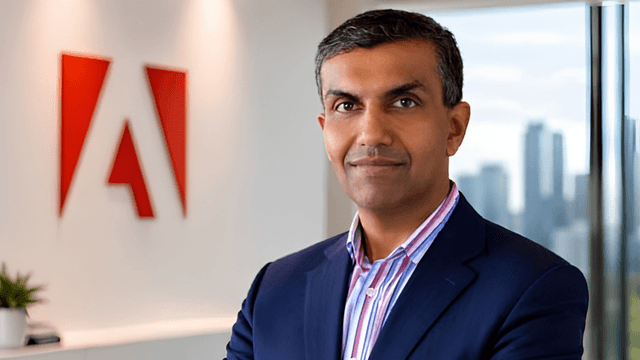 Business professional stands in front of an Adobe logo in an office setting