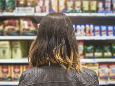 Person with shoulder-length hair facing shelves stocked with various packaged food items