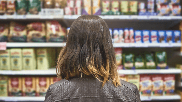 Person with shoulder-length hair facing shelves stocked with various packaged food items