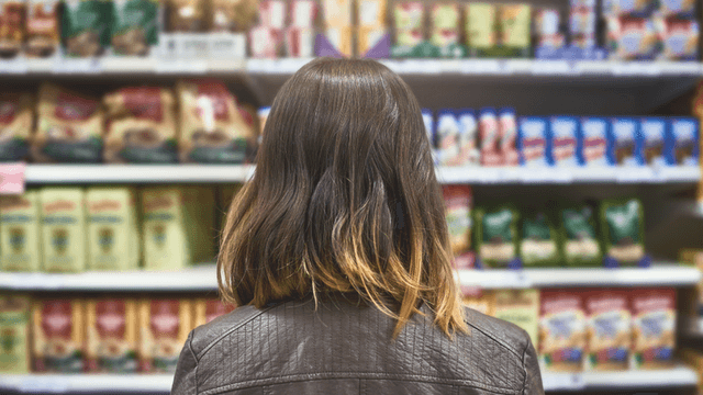 Person with shoulder-length hair facing shelves stocked with various packaged food items