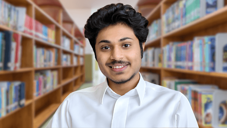 Young man in a white shirt smiling in a library setting with bookshelves