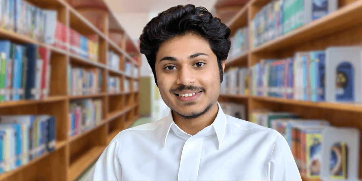 Young man in a white shirt smiling in a library setting with bookshelves