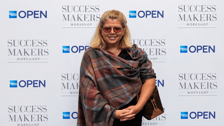 Smiling woman in sunglasses poses in front of a branded backdrop at an event