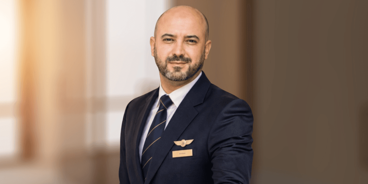 Man in a suit with a pilot's badge standing confidently in a blurred background