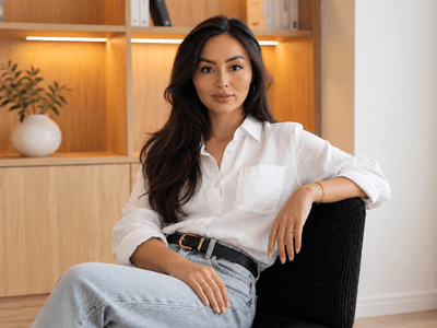 A woman with long dark hair sits confidently in a modern, minimalistic room