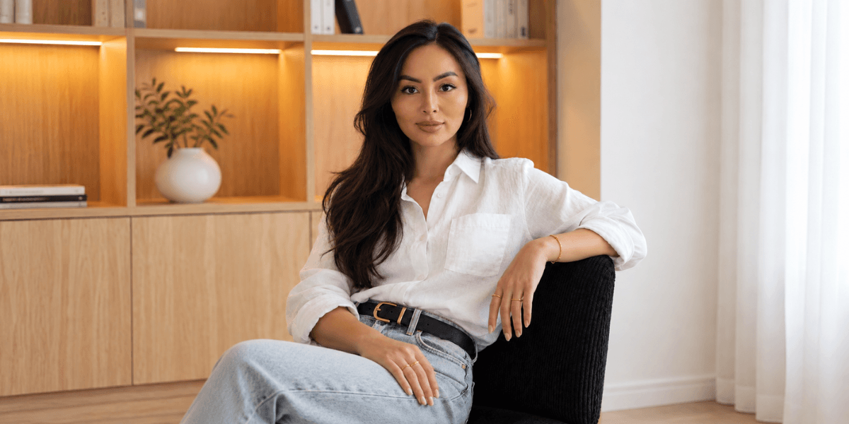 A woman with long dark hair sits confidently in a modern, minimalistic room
