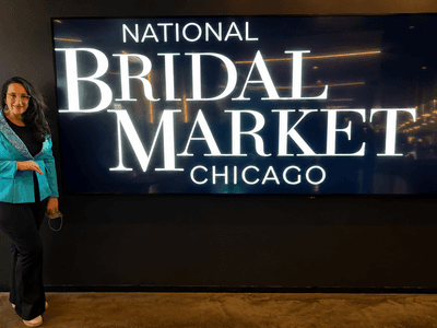 Person in a teal blazer poses beside a large screen displaying "National Bridal Market Chicago"