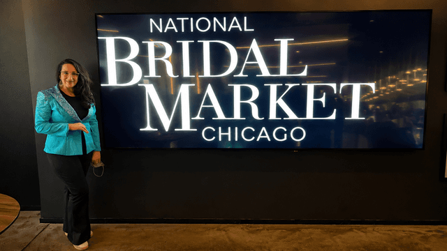 Person in a teal blazer poses beside a large screen displaying "National Bridal Market Chicago"