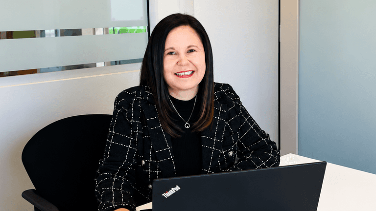 A woman sitting at a desk with a laptop, smiling confidently in an office setting