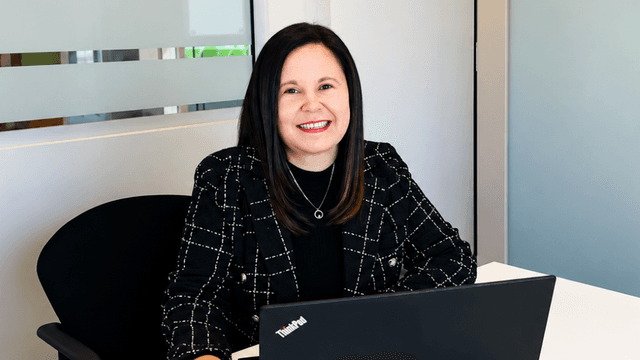 A woman sitting at a desk with a laptop, smiling confidently in an office setting