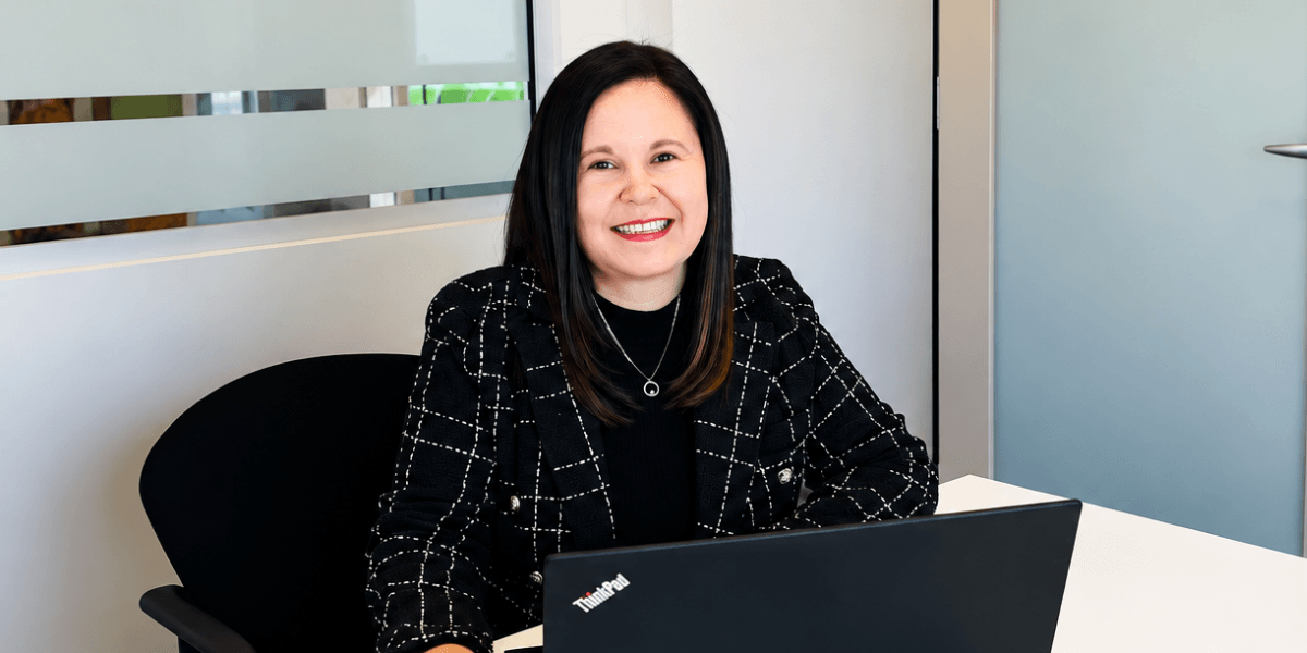 A woman sitting at a desk with a laptop, smiling confidently in an office setting