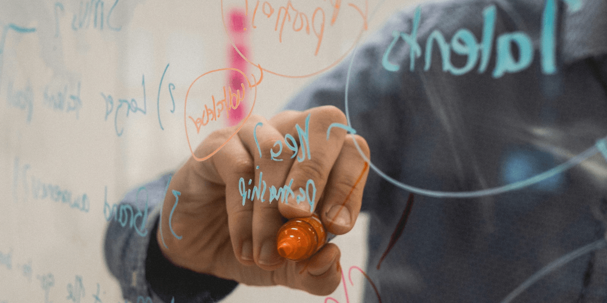 Person writing on a glass board with colorful markers and brainstorming ideas