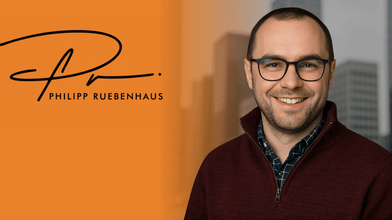 Professional portrait of a smiling man in a burgundy sweater with a city backdrop