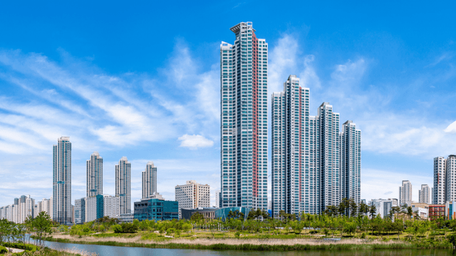 Modern high-rise buildings reflecting in a serene waterfront with blue sky and clouds