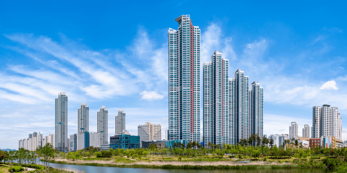 Modern high-rise buildings reflecting in a serene waterfront with blue sky and clouds