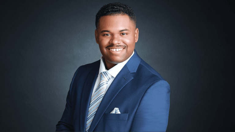 Smiling man in blue suit and tie, professional headshot against dark background.