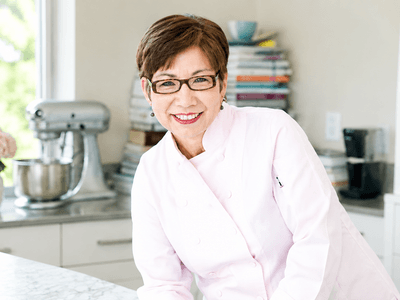 Angela McCrovitz smiling in a chef's coat inside a bright kitchen.