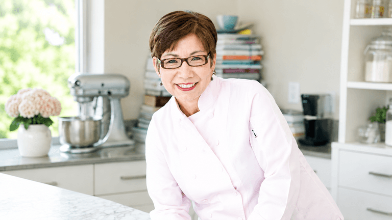 Angela McCrovitz smiling in a chef's coat inside a bright kitchen.