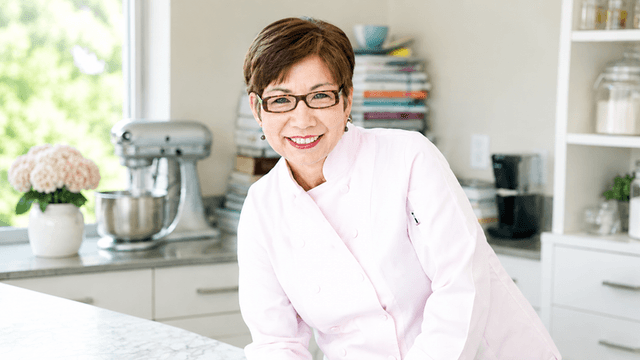 Angela McCrovitz smiling in a chef's coat inside a bright kitchen.