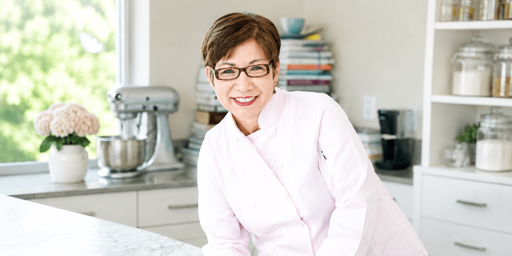 Angela McCrovitz smiling in a chef's coat inside a bright kitchen.