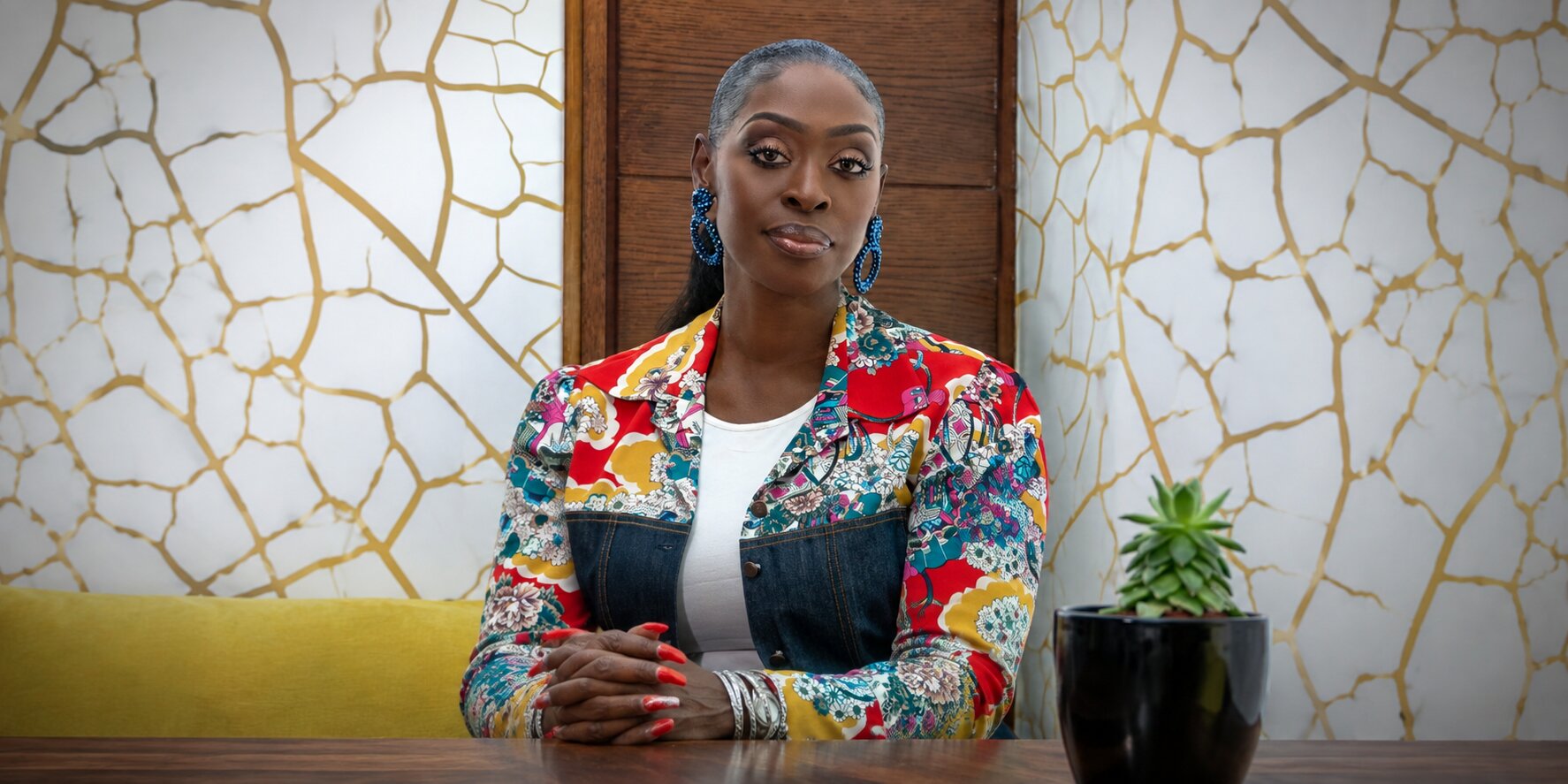 Dilys Sillah seated at a table wearing a colorful jacket in a contemporary office setting.