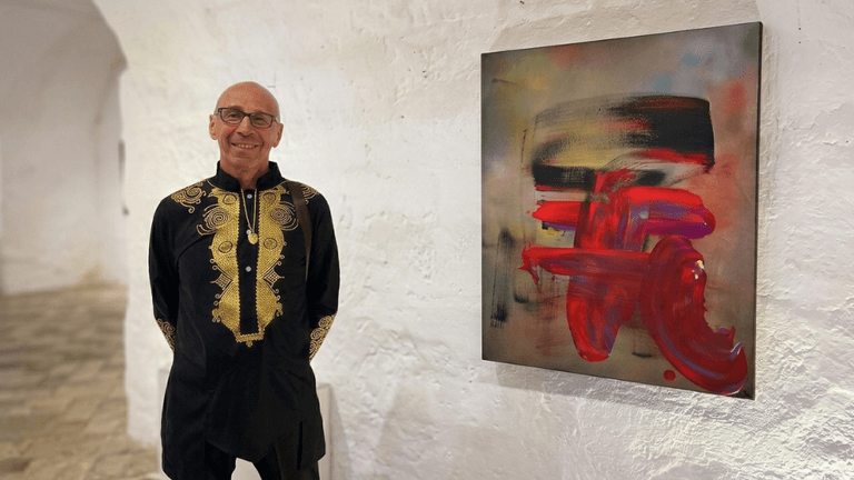 Marc Noël standing beside a vibrant abstract quantum painting at a contemporary art exhibition.